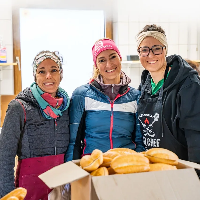 Drei Frauen stehen in einer Küche mit einer Kiste Brot vor ihnen.