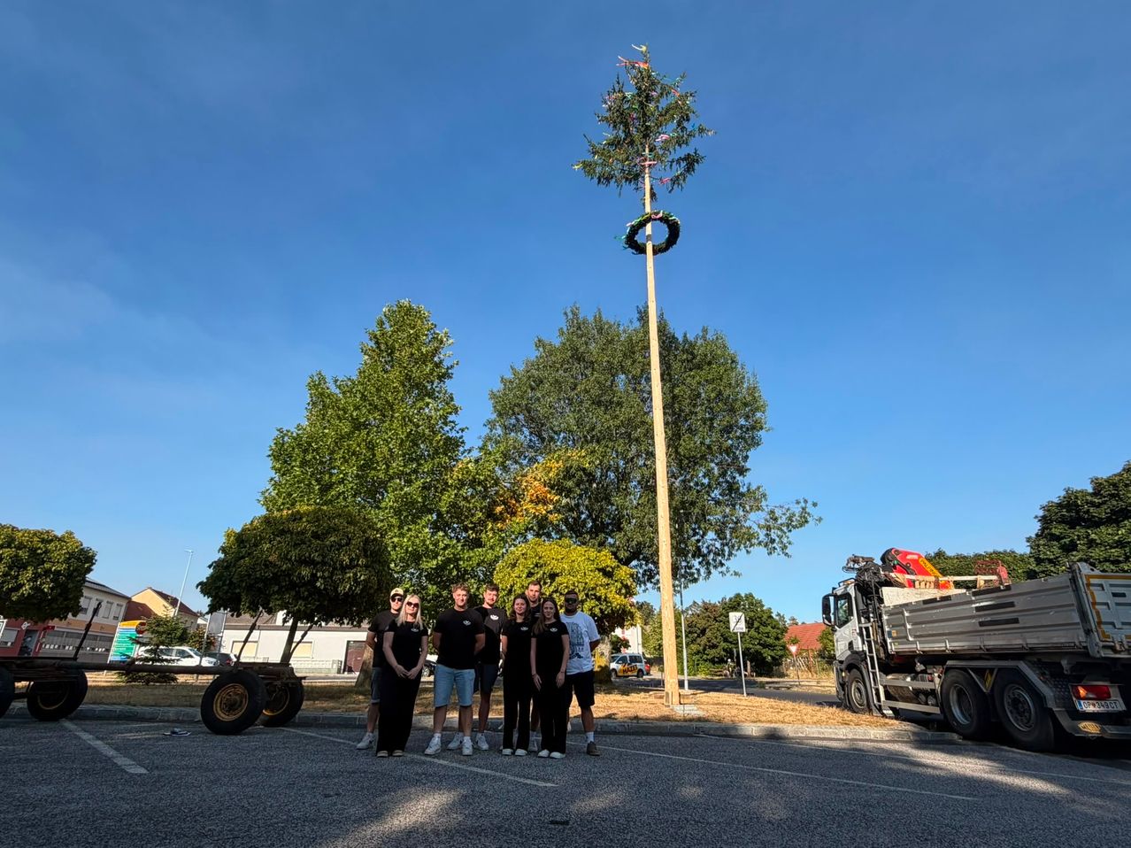 A group of people stands in front of a tall, decorated tree in a park, with a truck parked nearby.