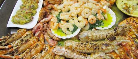 Eine Auswahl an Meeresfrüchten, darunter Garnelen und Hummer, auf weißen Tellern angeordnet. Einige Garnelen sind mit grünem Gemüse serviert.