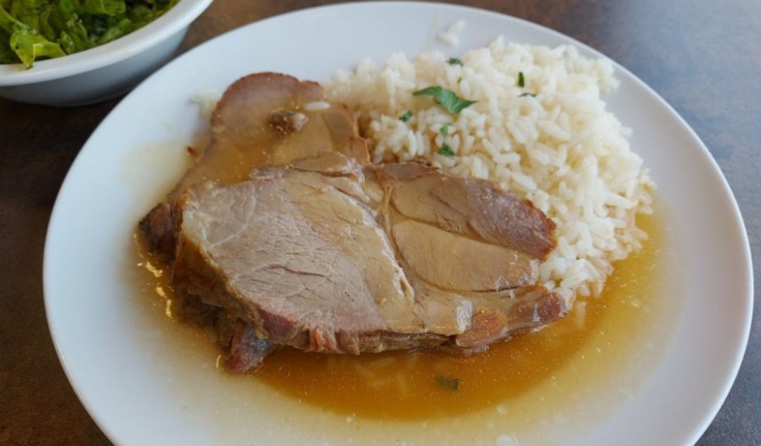 Auf einem Teller befinden sich geschnittene Schweinefleischstücke mit Reis und Sauce. Das Schweinefleisch ist mit Kräutern garniert und wird von einer Beilage aus weißem Reis begleitet.