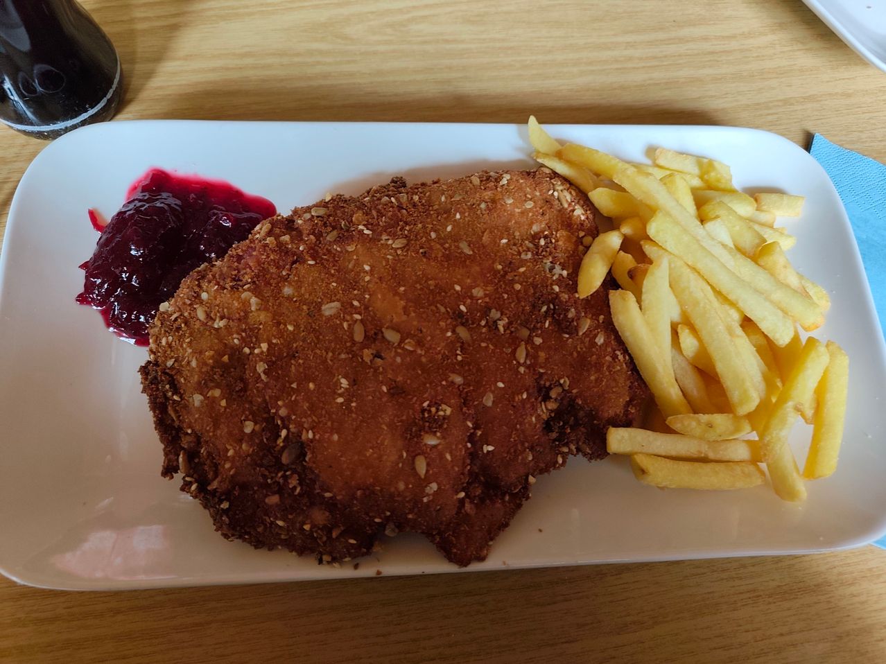 A white plate with fried breaded meat, French fries, and cranberry sauce on a wooden table.