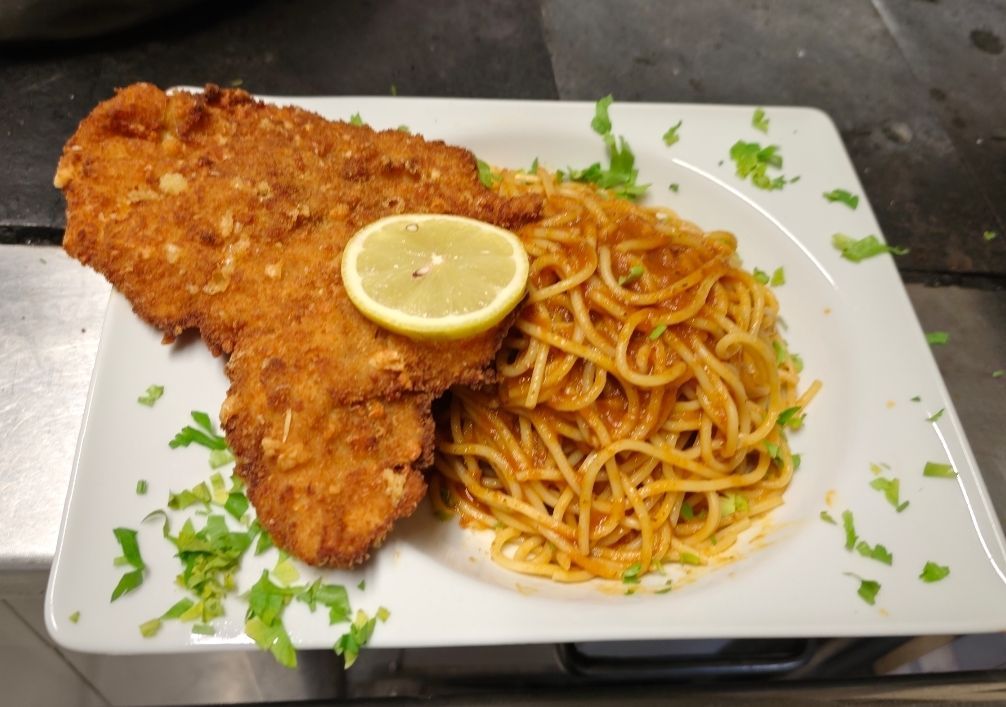 Ein Teller mit gebratenem, paniertem Fleisch, Spaghetti und einer Zitronenscheibe, garniert mit Petersilie.