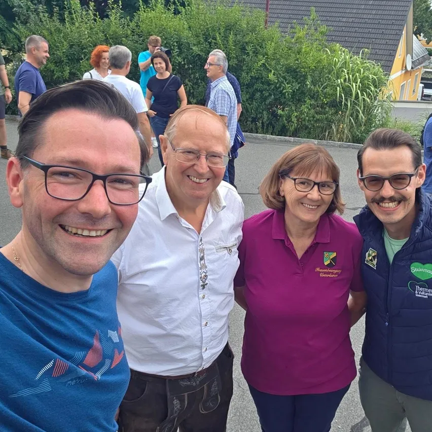Vier Menschen lächeln und posieren für ein Foto im Freien. Sie stehen vor einem Haus mit gelber Wand.