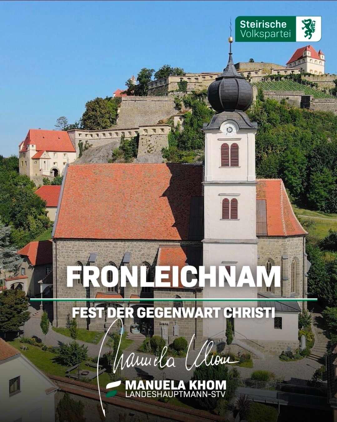 A church named Fronleichnam is shown in the picture with a tower and a red roof. Behind it, there are trees and a castle on top of the hill.