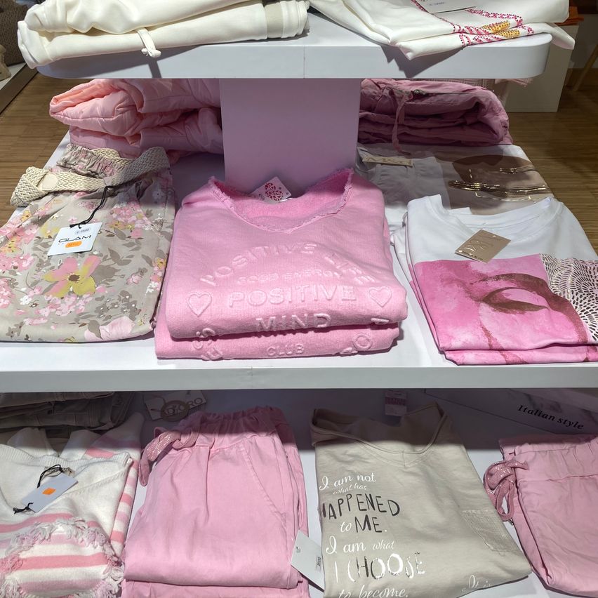A shelf with children’s clothing displayed. Pink tops with ‘I am positive’ and ‘I choose to become’ text. Other clothes folded neatly.