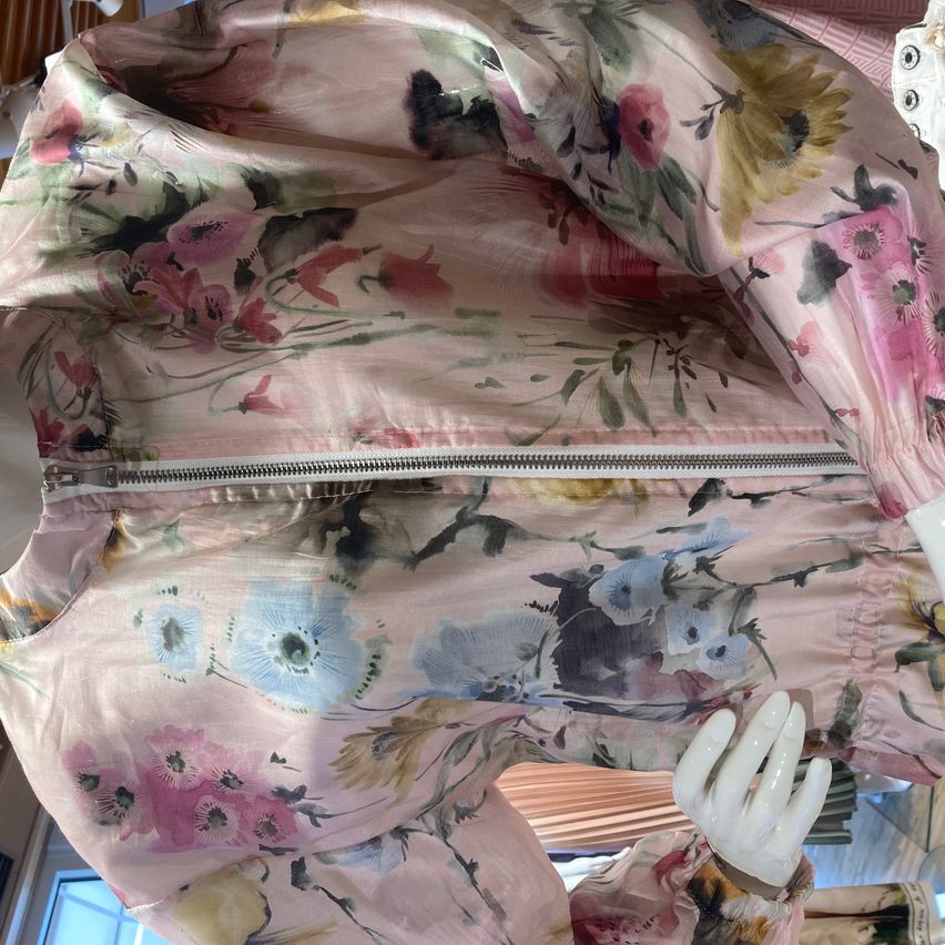 A floral print dress with pink, blue, and yellow flowers on a white mannequin. The dress has a zipper on the front.