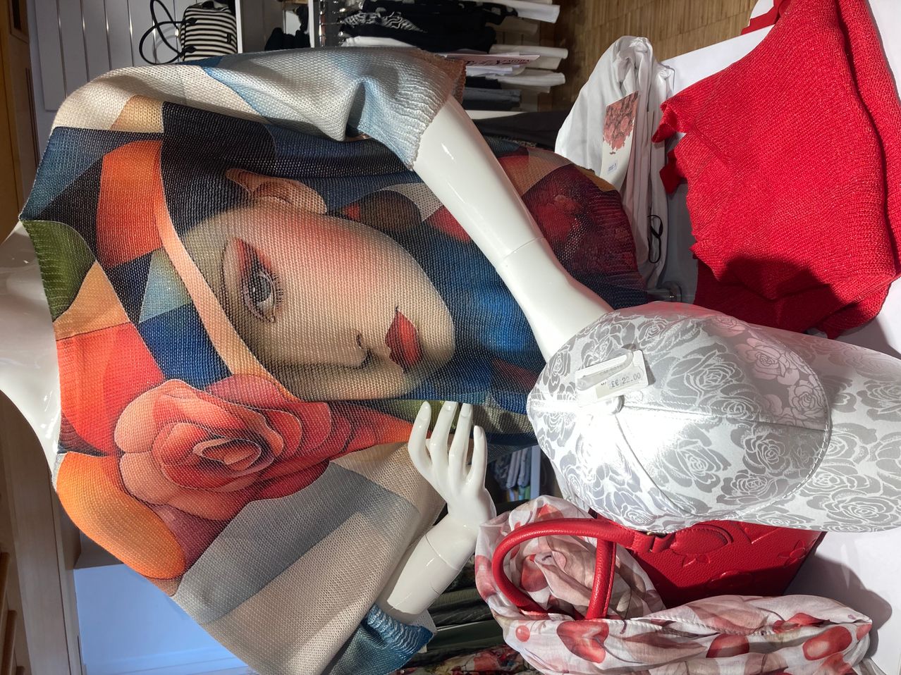 A mannequin with a dress featuring a portrait of a woman with a hat and rose, also holding a hat and handbag.