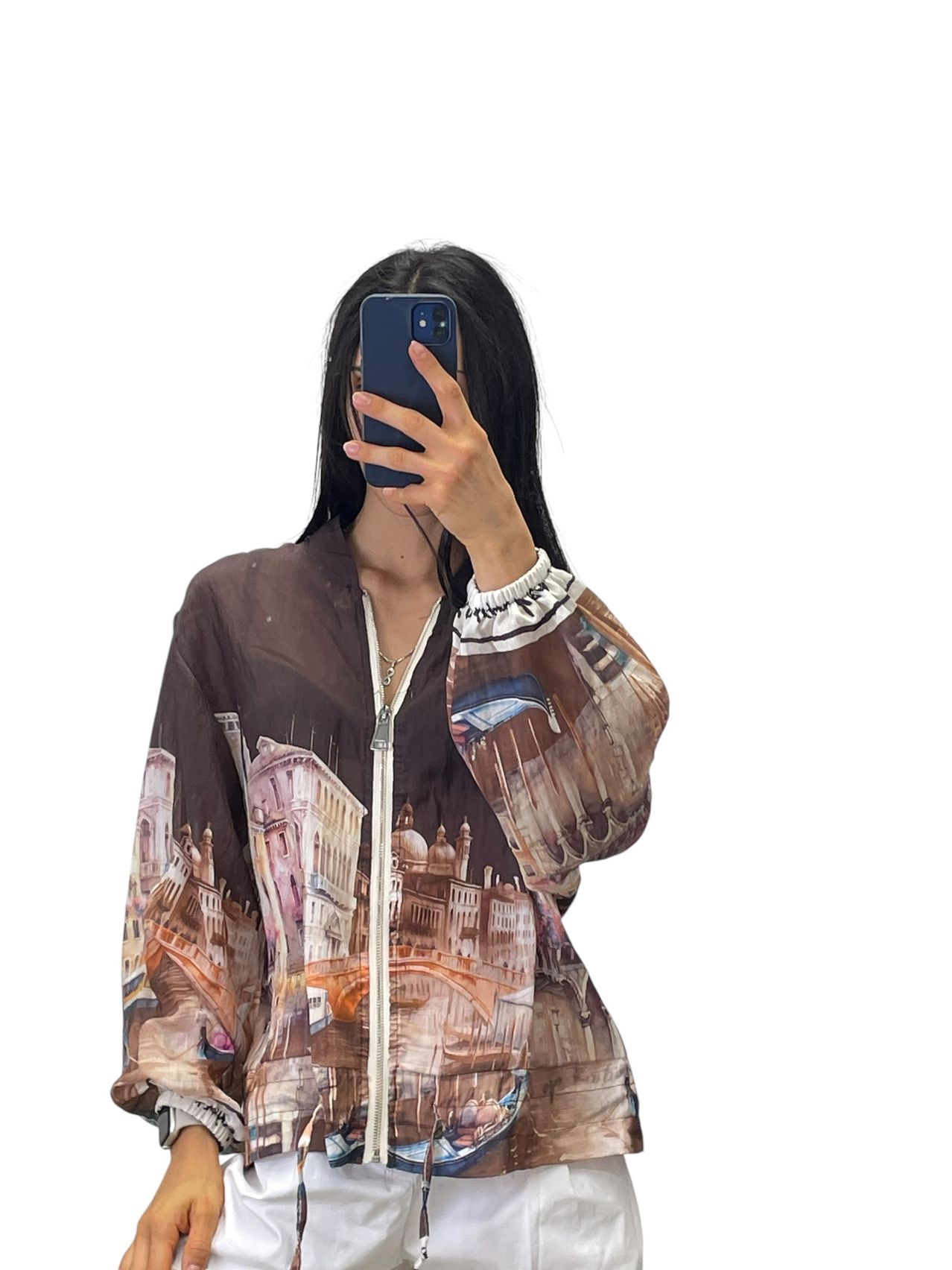 A woman takes a selfie with a phone, wearing a jacket with a cityscape print.