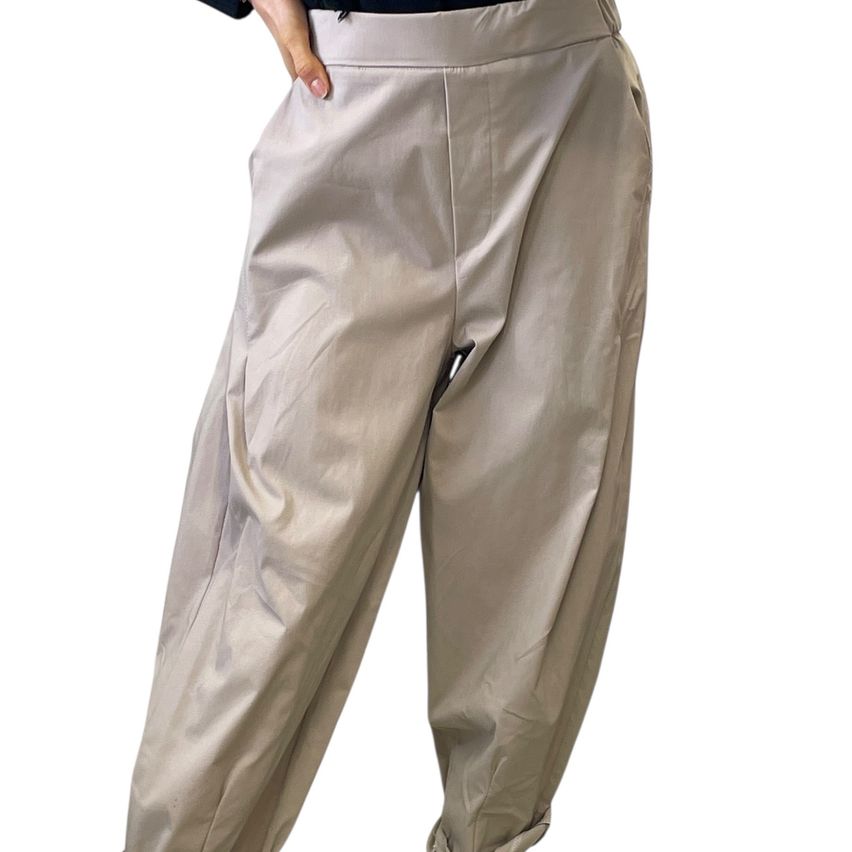 A person wearing beige wide-leg pants with a slightly shiny fabric texture, shown from the waist down with a hand holding the waistband.