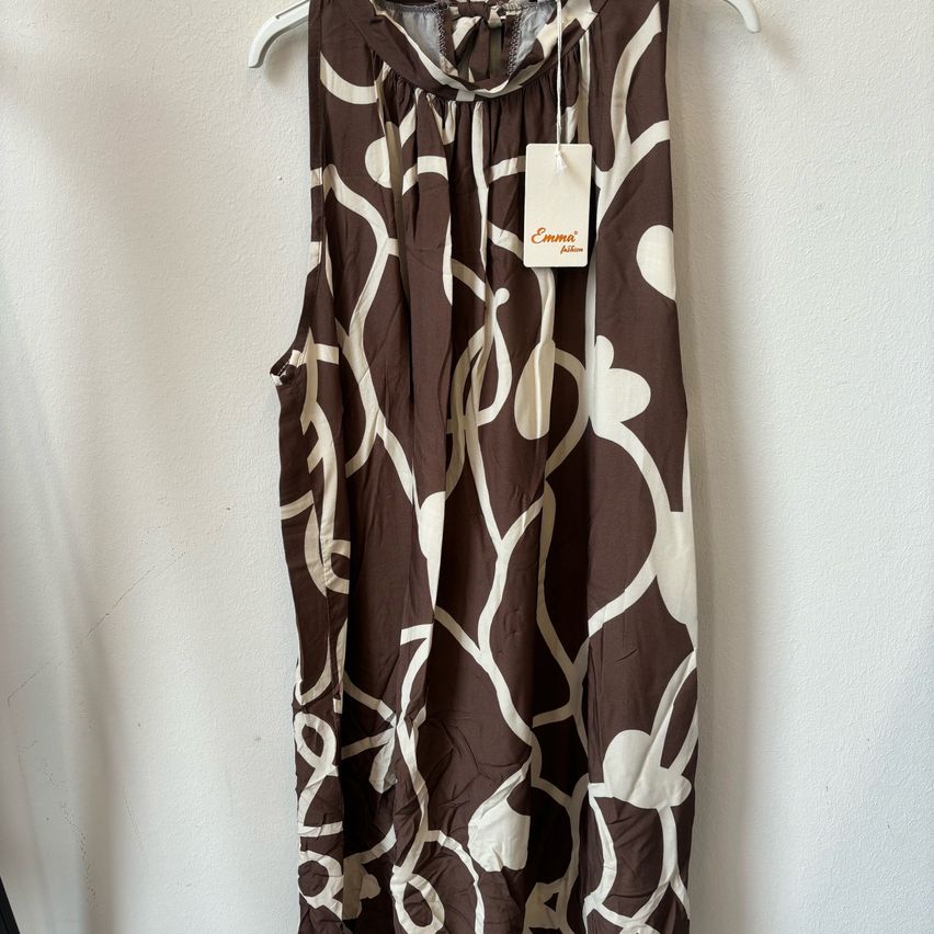 Ein ärmelloses braun-weiß gemustertes Kleid hängt an einer weißen Wand mit einem weißen Etikett, das Emma's Fashion liest.