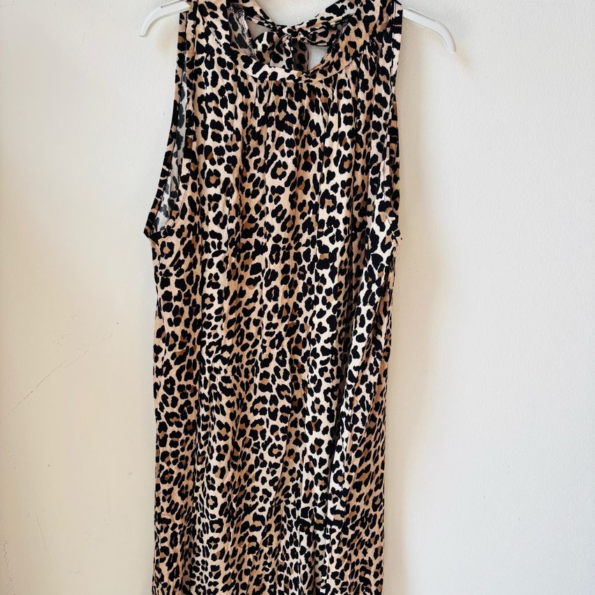 Ein Leopardendruckkleid mit einem Halsausschnitt hängt an einem weißen Kleiderbügel an einer schlichten weißen Wand.