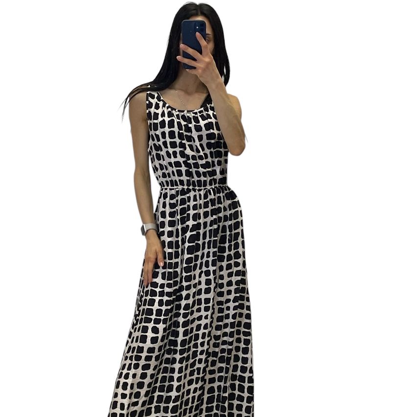 A woman takes a selfie in a black and white patterned dress, against a white background.
