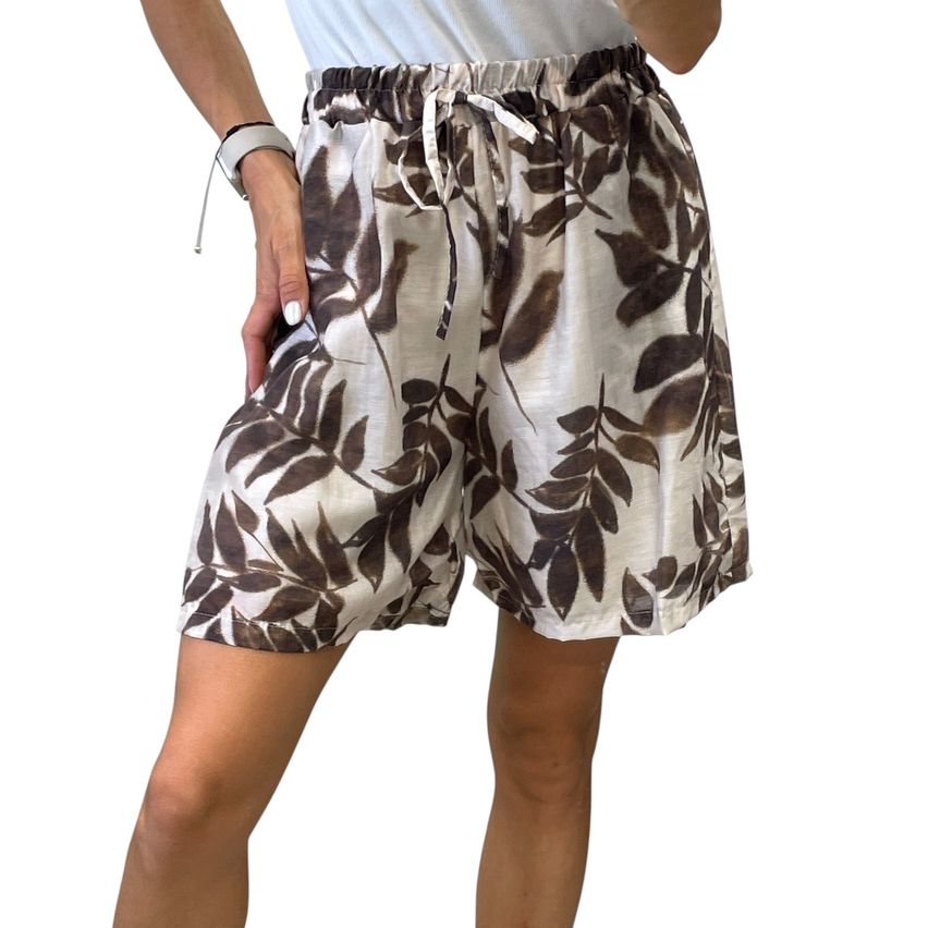 A woman wears a pair of high-waisted, light brown shorts with a leaf pattern, held up by a drawstring. Her right hand rests on her hip.