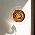 Ein Nahaufnahme eines Weinglases, gefüllt mit einer rötlichen Flüssigkeit, auf einer weißen Oberfläche mit Sonnenlicht, das Reflexionen und Schatten erzeugt.