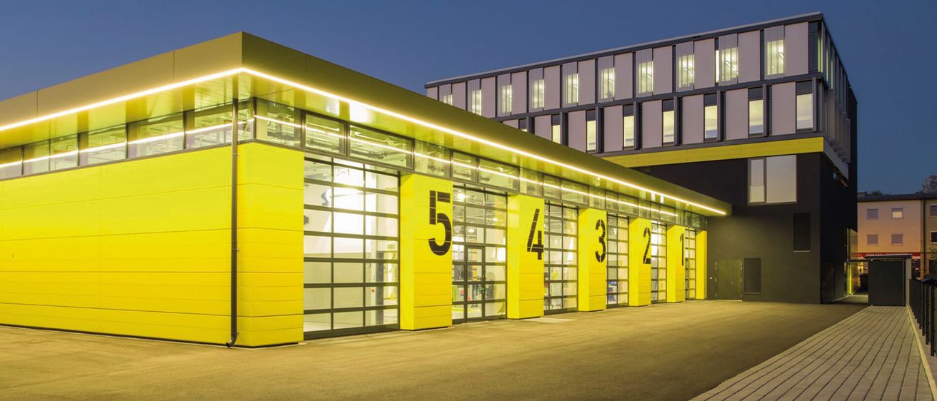 Ein modernes Gebäude mit gelben Außenwänden, Glastüren und -fenstern sowie nummerierten gelben Säulen. Die Zahlen 5, 4, 3, 2 und 1 sind auf den Säulen sichtbar.