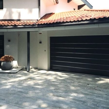 Ein Außenansicht eines modernen Hauses mit Garage und einem Pflanzentopf auf der Einfahrt. Die Garagentür ist schwarz und geschlossen.