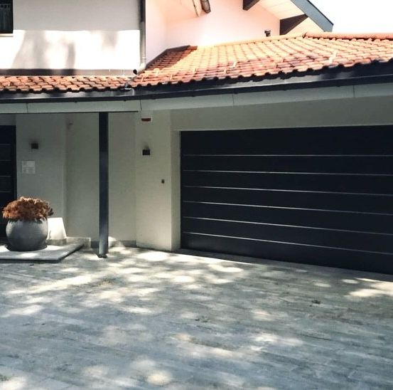 Ein Außenansicht eines modernen Hauses mit Garage und einem Pflanzentopf auf der Einfahrt. Die Garagentür ist schwarz und geschlossen.