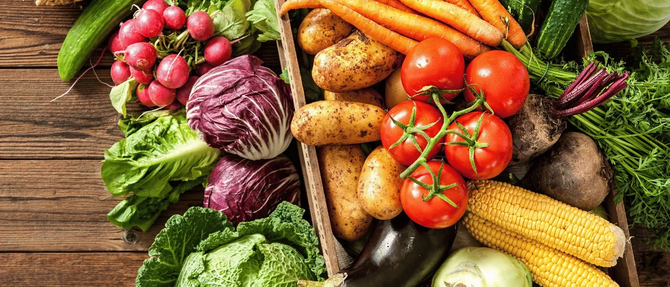 Ein Holzkasten gefüllt mit verschiedenen Gemüsesorten, darunter Karotten, Kartoffeln, Tomaten und Kohl.