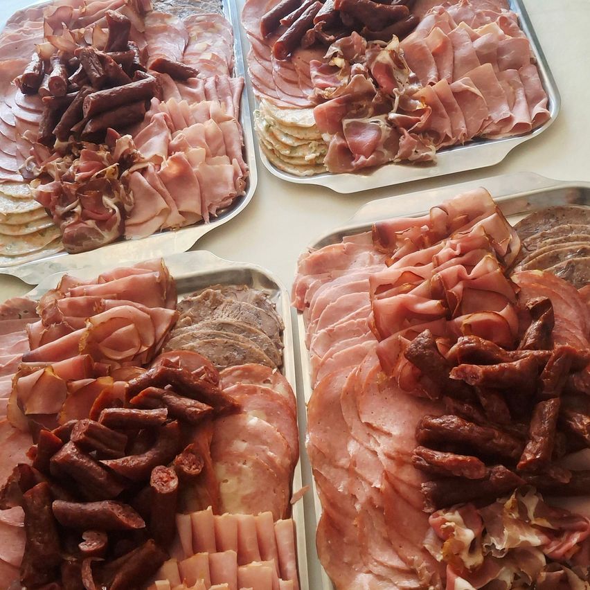 Vier Tabletts mit verschiedenen Sorten von Wurstwaren sind auf einem Tisch ausgestellt, einschließlich Scheiben von Salami, Schinken und anderen Würsten.
