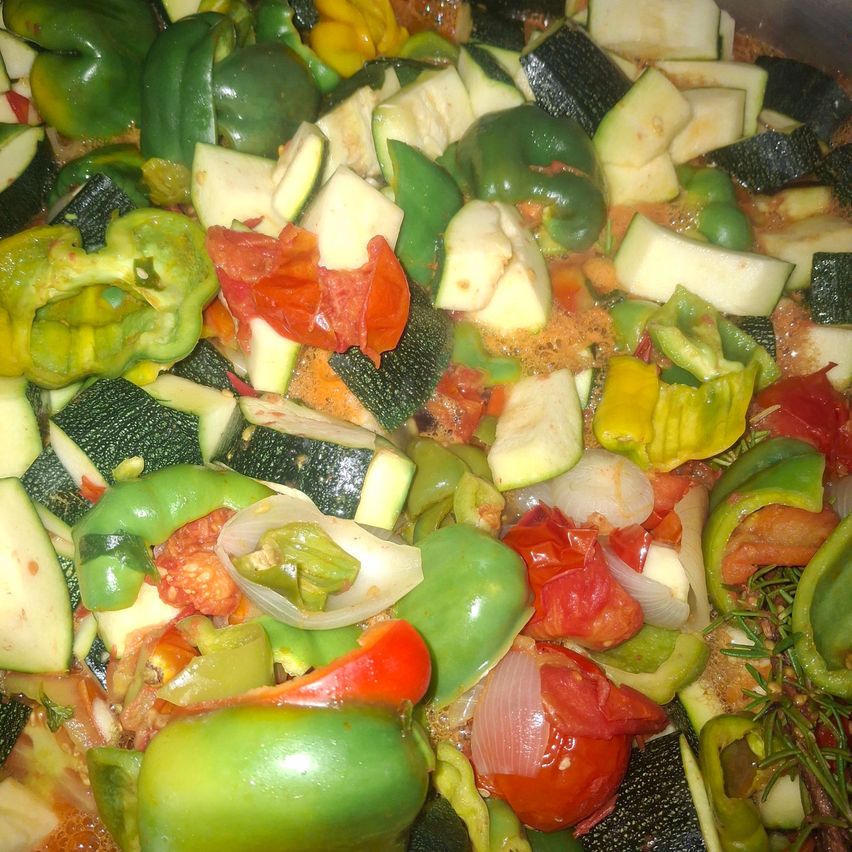 Eine Nahaufnahme eines Topfes mit einer Mischung aus gehackten Gemüsen, einschließlich grüner Paprika, Zucchini, Tomaten und Zwiebeln.