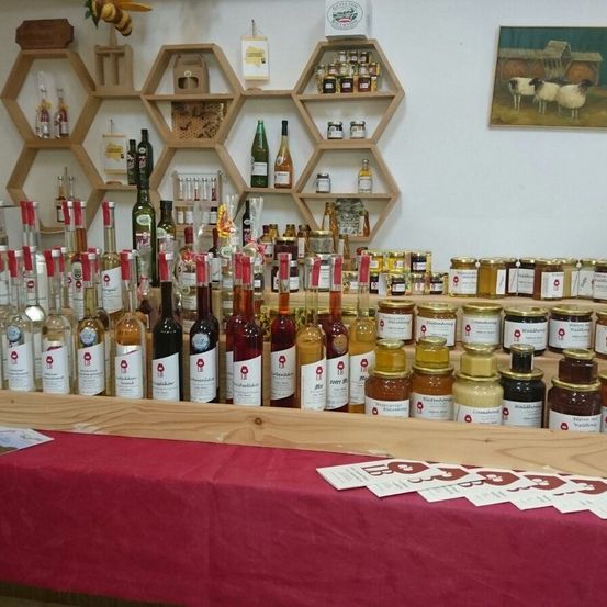 Ein Tisch zeigt verschiedene Honigflaschen, in Reihen angeordnet. Dahinter haben Regale mit sechseckigen Fächern mehr Honiggläser und Flaschen. Ein Gemälde von Schafen schmückt die Wand.