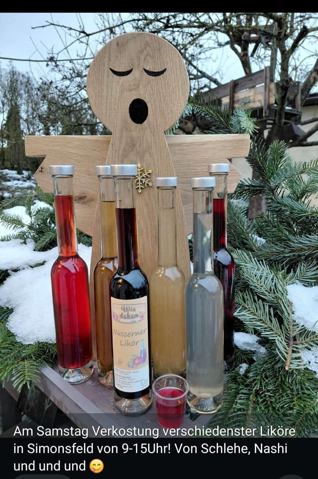 Flaschen mit Liköretiketten sind in einer Reihe angeordnet, vor einer hölzernen Weihnachtsdekoration mit Schnee.