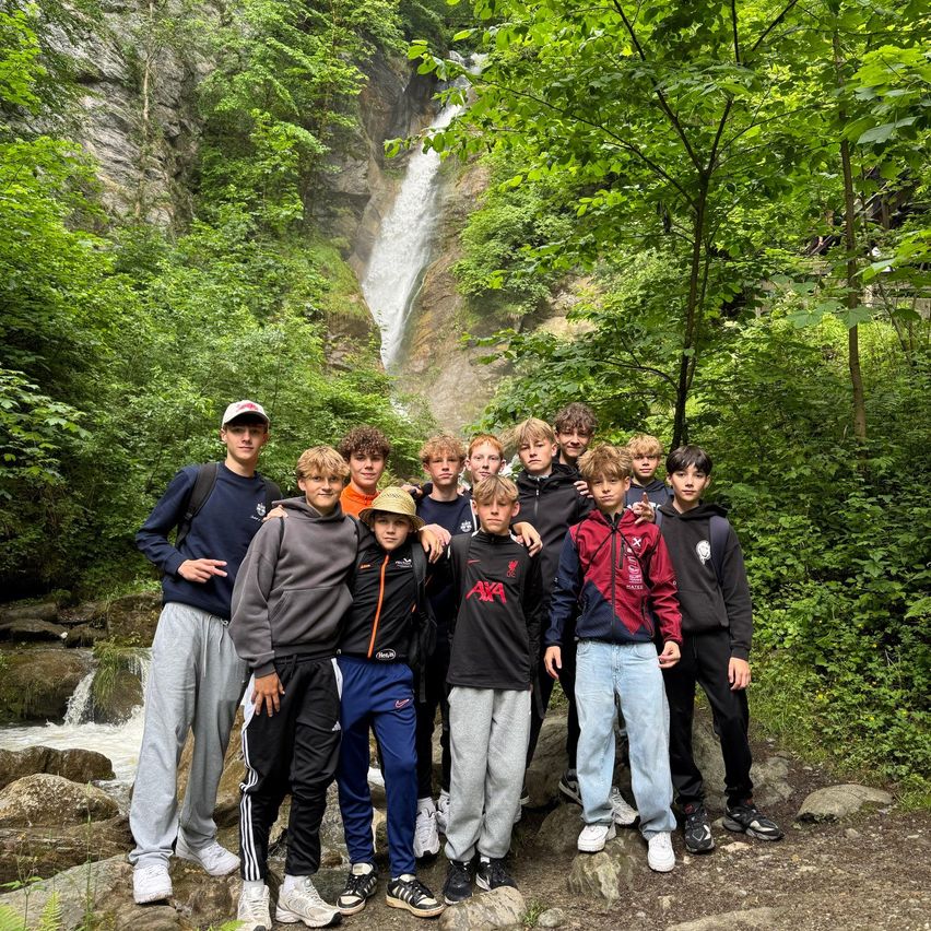 Eine Gruppe von Jungen in Jacken und Hosen posiert für ein Foto vor einem Wasserfall mit Felsen und Grün.