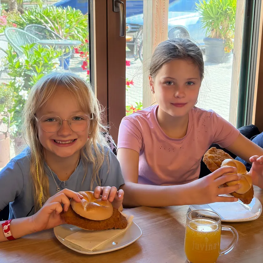 Zwei Mädchen sitzen an einem Tisch in einem Restaurant und halten ein Sandwich und ein Brötchen.