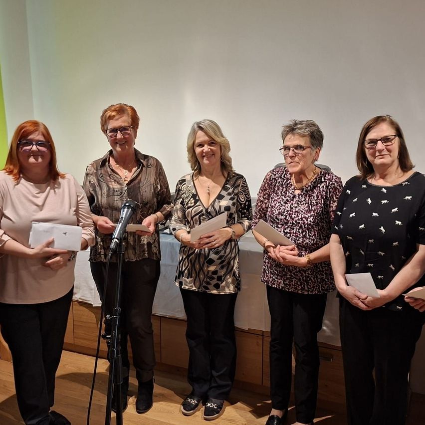 Fünf Frauen stehen hinter einem Podium mit einem Mikrofon und halten Papiere in den Händen. Sie scheinen für ein Foto zu posieren. Hinter ihnen ist eine weiße Wand und eine weiße Tischdecke.