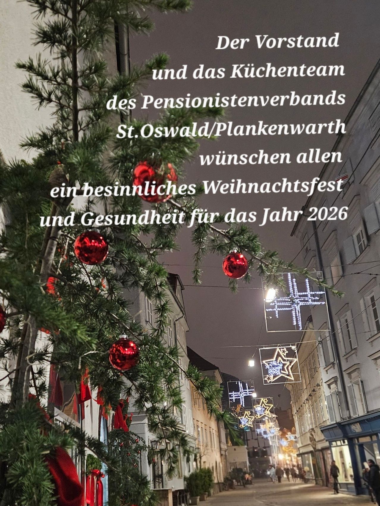 Ein Weihnachtsbaum mit roten Kugeln ist vor einem Gebäude mit einem Schild dekoriert. Der Text lautet: 'Das Küchenteam des Pensionistenverbandes St. Oswald/Plankenwarth wünscht allen ein besinnliches Weihnachtsfest und Gesundheit für das Jahr 2026.'