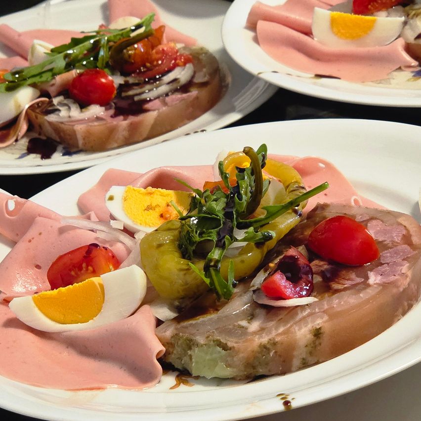 Drei weiße Teller mit Fleischscheiben, Eiern, Tomaten, grünem Gemüse und Brot. Das Fleisch ist geschnitten und auf dem Brot platziert. Die Eier sind halbiert. Die Tomaten sind ganz und geschnitten.