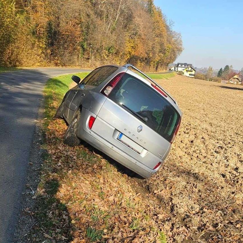 Ein silberner Renault Scenic ist an der Seite einer Landstraße geparkt, zur Straßenseite hin geneigt, mit umliegenden gefallenen Blättern.