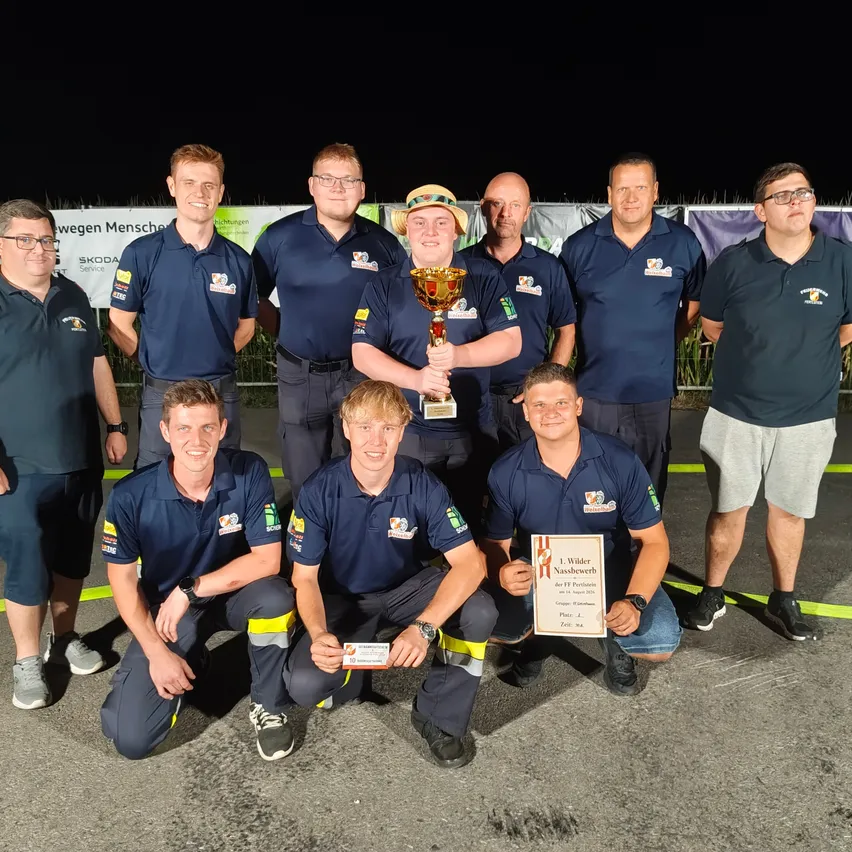 Eine Gruppe von Männern in blauen Uniformen posiert für ein Foto mit einem Pokal und Zertifikaten. Sie stehen auf einer Betonfläche mit gelben Linien.