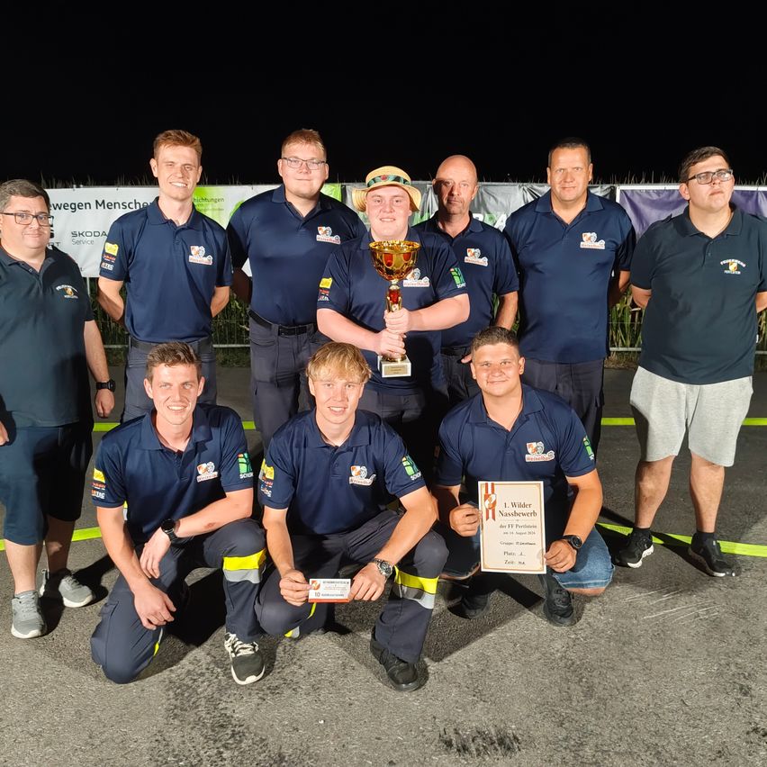 A group of men in blue uniforms are posing for a photo with a trophy and certificates. They are standing on a concrete surface with yellow lines.