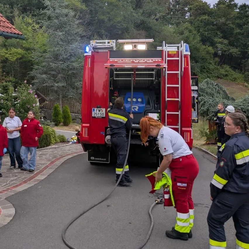 Eine Gruppe von Feuerwehrleuten bereitet einen Feuerwehrwagen mit Schlauch und Leiter auf einer gepflasterten Straße vor.