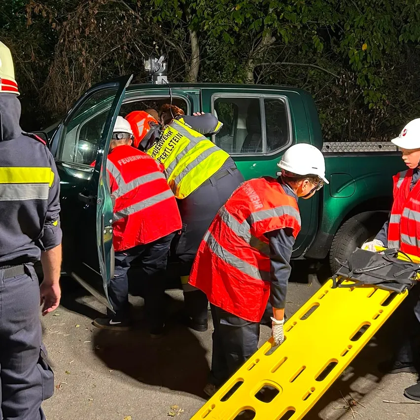 Rettungskräfte in reflektierenden Westen und Helmen helfen einer Person aus einem grünen Pickup-Truck mit einer Trage.