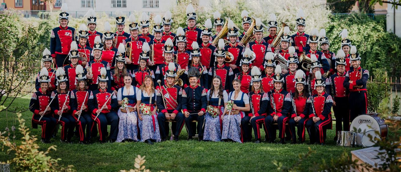 Ein Marschkapelle posiert für ein Gruppenfoto vor einem historischen Gebäude mit vielen Fenstern und rotem Rand.