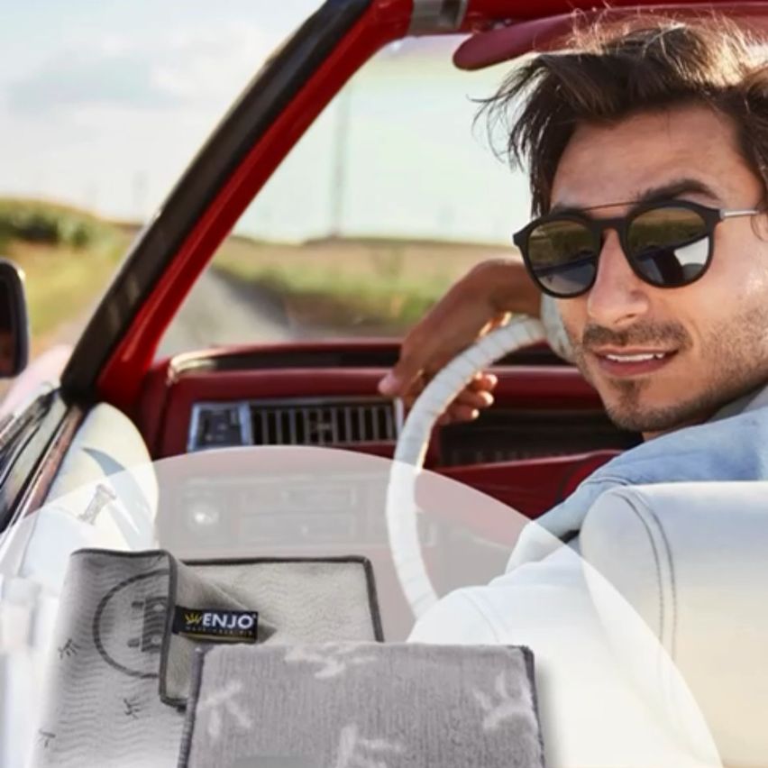Ein Mann fährt ein rotes Cabrio mit Sonnenbrille, einem Lächeln im Gesicht und zwei grauen Reinigungstüchern im Vordergrund.