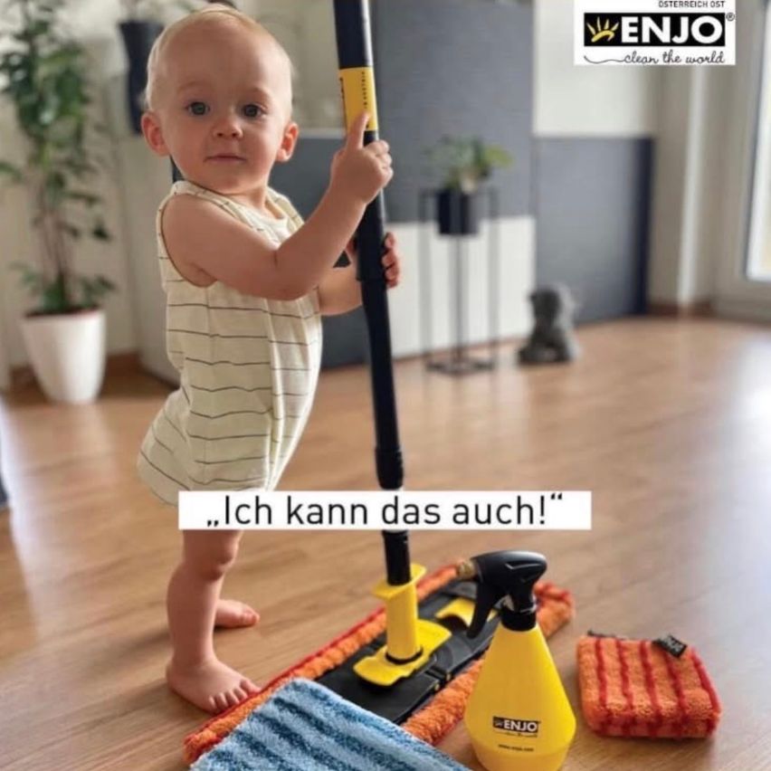 Ein Kleinkind in einem gestreiften Strampler steht auf einem Holzboden und hält einen Mop und eine Sprühflasche. Im Hintergrund befinden sich Topfpflanzen und eine weiße Wand. Das Bild enthält einen deutschen Textüberlagerung '...Ich kann das auch!'.
