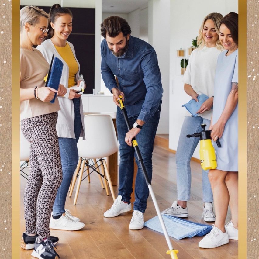 Fünf Personen reinigen den Boden in einem Raum, ein Mann wischt den Boden, während andere zusehen und Reinigungswerkzeuge in der Hand halten.