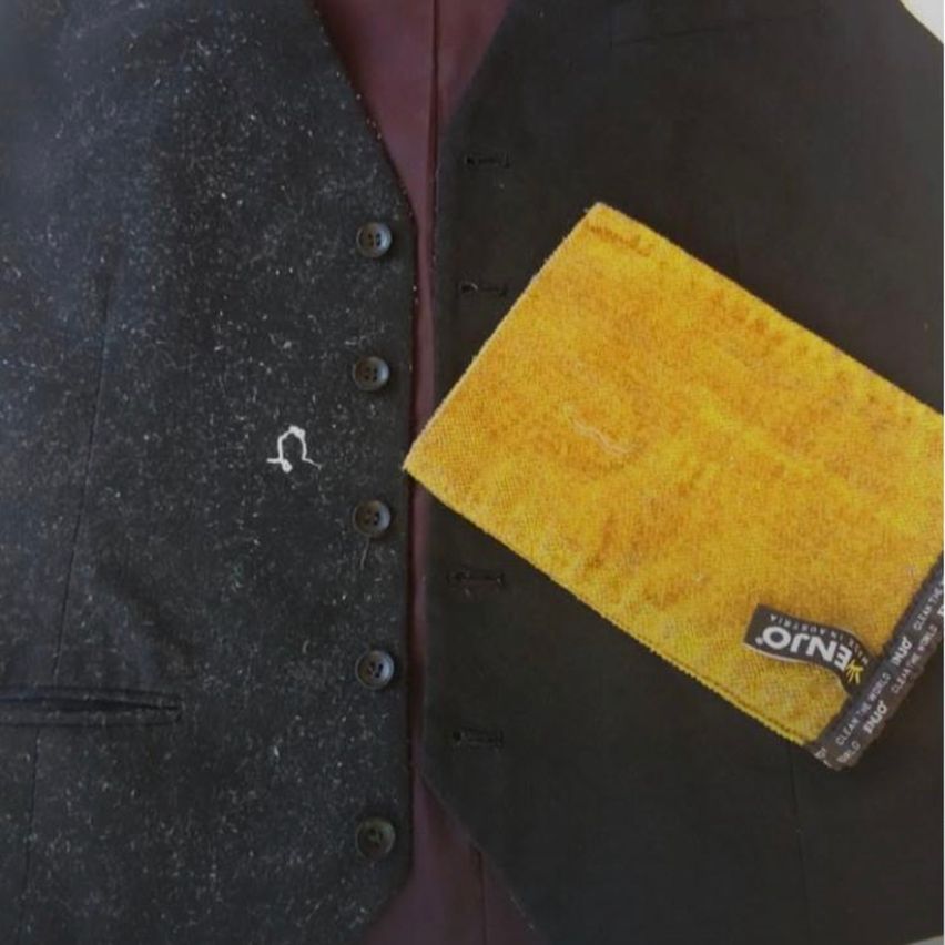 Ein schwarzer Weste mit einem gelben Mikrofasertuch darauf. Das Tuch hat ein Logo, das 'Ban.' liest. Die Weste hat mehrere Knöpfe.