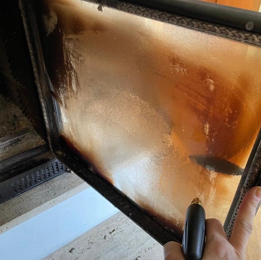 Eine Person reinigt eine Glasscheibe mit einer Bürste, die Scheibe weist Brandflecken und Flecken auf.