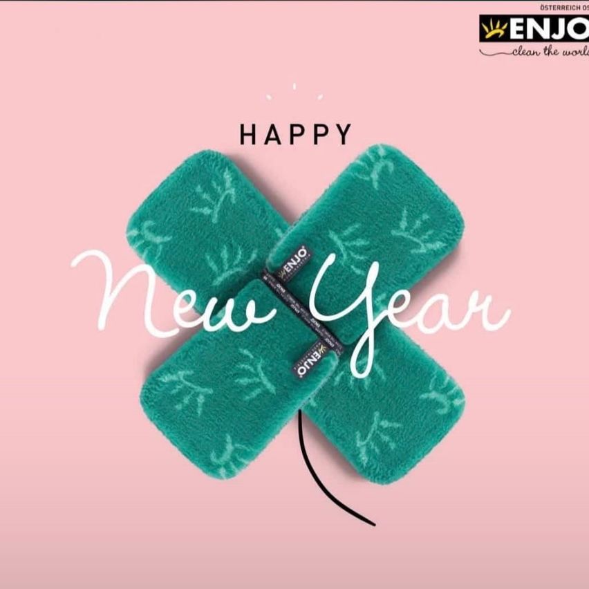 Ein Bild mit rosa Hintergrund zeigt zwei grüne ENJO Schwämme in Kreuzform mit dem Text 'GLÜCKLICHES NEUES JAHR' darüber. Die Schwämme haben ein weißes Design.