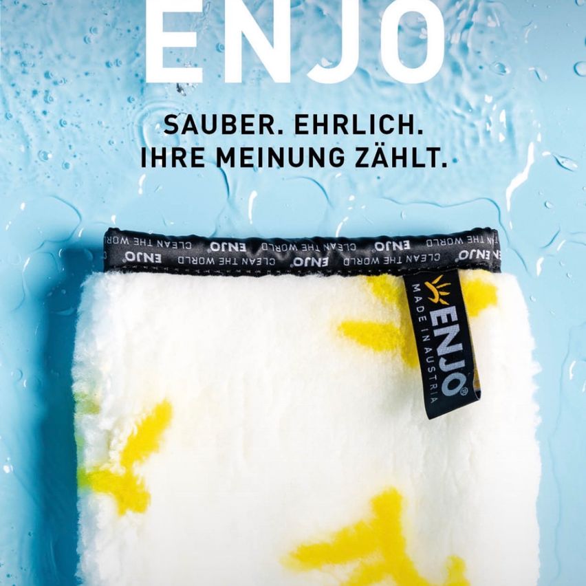 Werbung für ENJO mit einem weißen Handtuch mit gelben Flecken und einem blauen Hintergrund mit Wassertropfen. Der Markenname und Slogan sind prominent angezeigt.