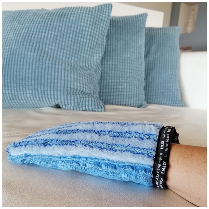 Ein Nahaufnahme eines blau-weißen Mikrofaser-Reinigungstuchs mit einem Armband auf einem Bett mit blauen Kissen im Hintergrund.