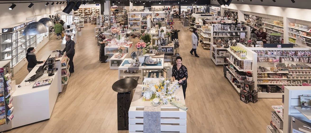 Ein geräumiges Inneres eines Einzelhandelsgeschäfts mit Holzböden, Deckenbeleuchtung und zahlreichen ausgestellten Produkten. Mehrere Kunden stöbern durch die Artikel.