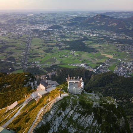 Luftaufnahme eines Aussichtsturms auf einem Berggipfel mit einer Stadt unten. Der Turm hat einen Turm und Solarpanele.