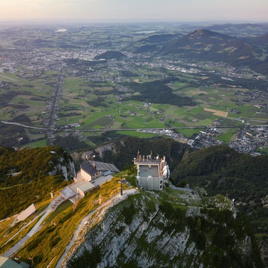 Aerial view of a lookout tower on top of a mountain with a city below. The tower has a tower and solar panels.