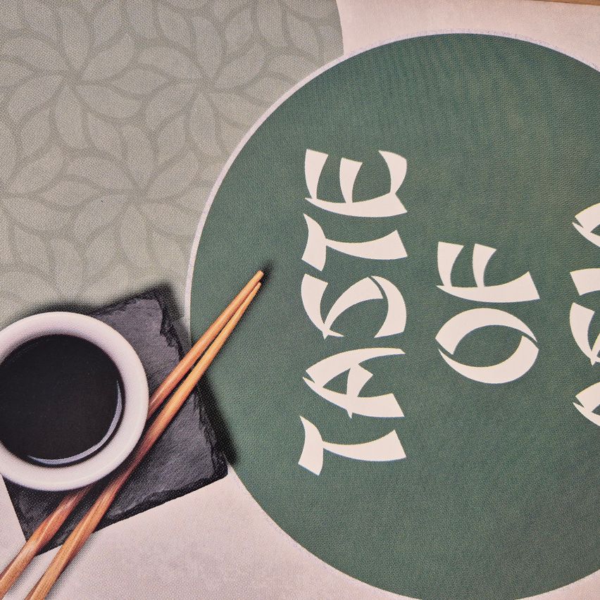Eine runde grüne Tischset mit 'Geschmack von Asien' in Weiß. Daneben ein Becher mit schwarzer Flüssigkeit, Chopsticks und ein schwarzer Untersetzer.