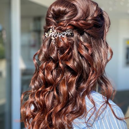 Eine Nahaufnahme einer Frau mit langen, gelockten braunen Haaren, die in einem Dutt gestylt sind und einen silbernen dekorativen Haarclip tragen. Sie trägt ein blaues gestreiftes Hemd.